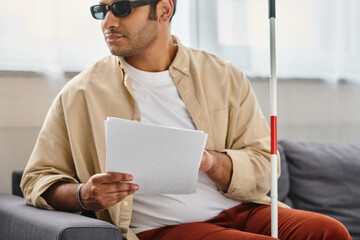merry indian man with visual impairment with glasses and walking stick reading braille code