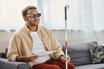 jolly indian man with visual impairment with glasses and walking stick reading braille code