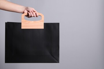 Woman holding paper shopping bag on grey background, closeup. Space for text