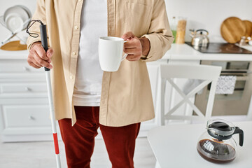 cropped view of indian man with blindness in cozy outfit holding walking stick and cup of coffee
