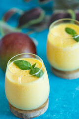 Fresh mango lassi in glasses on blue background with copy space.