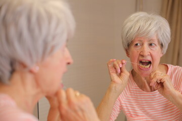 Senior woman presenting difficulties to floss her teeth 