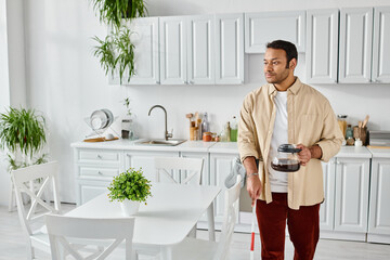 handsome indian man with blindness using walking stick and holding coffee pot while in kitchen