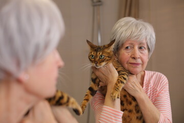 Senior woman holding her beautiful cat in the mirror 