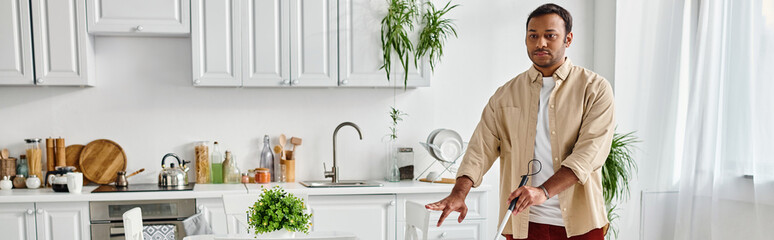 handsome blind indian man in cozy outfit using his walking stick while in his kitchen, banner