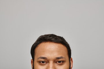 handsome indian male model looking contentedly straight at camera with gray wall on background