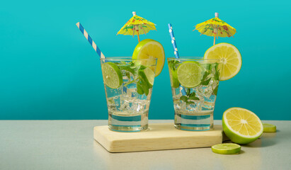 Two cocktails in glass  filled with ice and lemon slices garnished with lemon slices, yellow umbrellas and sorbets on a wooden board