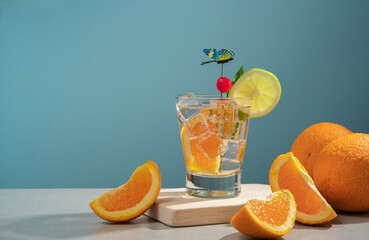Cocktail in glass glass filled with ice and orange slice garnished with lemon slice, cherry and butterfly pin on a wooden board with pieces of oranges