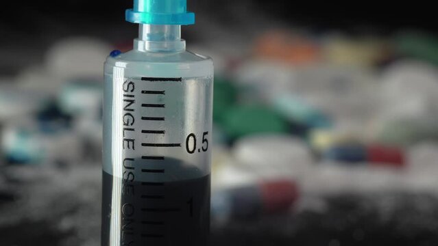 Close-up syringe plunger with blue liquid on the background of pills and medicines
