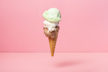 funny creative concept of flying wafer cone with sundae, pistachio and chocolate ice cream scoops on pink background