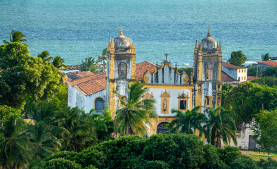 Fototapeta na wymiar Ancient coastal church surrounded by lush tropical forest in the old colonial town of Olinda, Recife, Brazil. A UNESCO World Heritage site