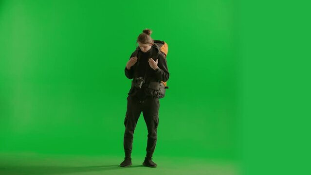 A male traveler takes pictures with a camera while hiking. A tourist with a backpack on his back stands full length in a studio on a green screen. Concept of travel, active rest, hiking.
