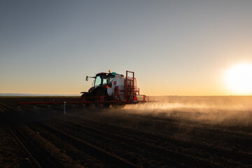 Tractor spraying land in sunset.