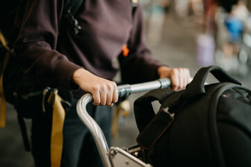 A close-up of an Asian woman's hand as she navigates a luggage cart, embarking on a domestic tour within the confines of the airport building.