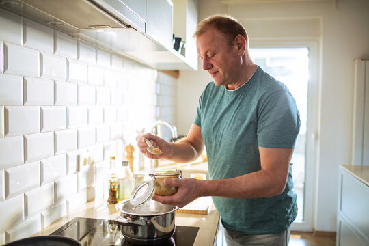 Middle aged man cooking and seasoning food in his kitchen