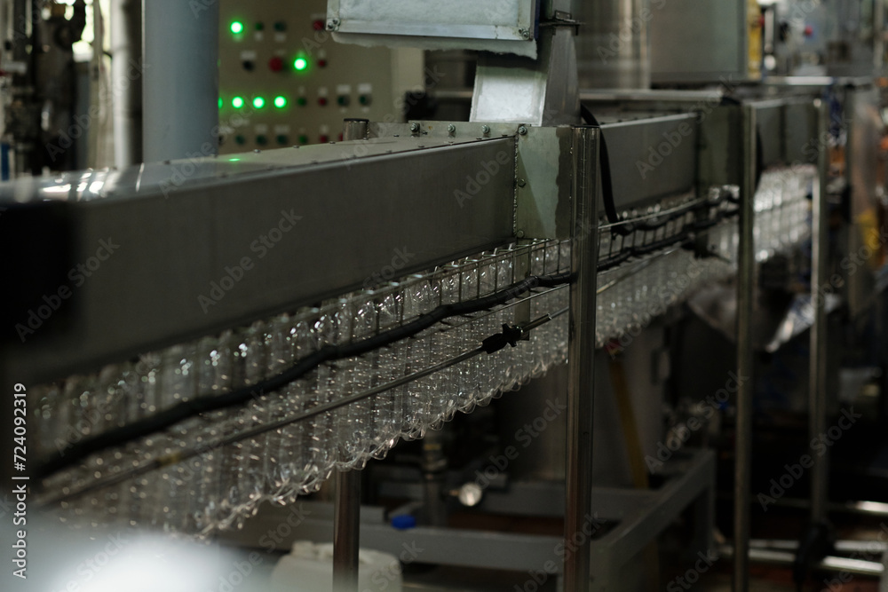 Aufkleber Part of belt conveyor with clean empty transparent plastic bottles moving along assembly line inside huge industrial machine in factory