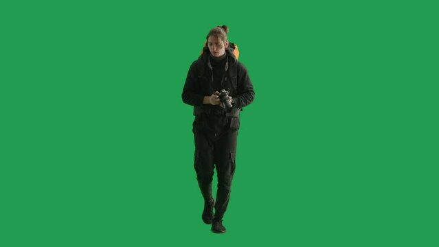 A male traveler takes pictures with a camera while hiking. Man hiker in full height walking in studio on green screen. Concept of travel, active rest, hiking.