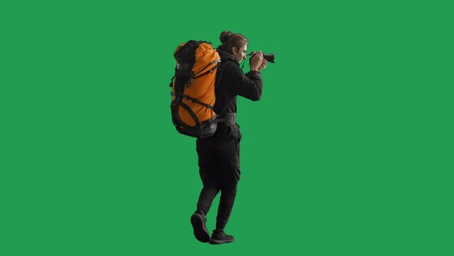 Back view of a male traveler taking photos on a camera during a hike. Man hiker in full length walking in studio on green screen. Concept of travel, active rest, hiking.