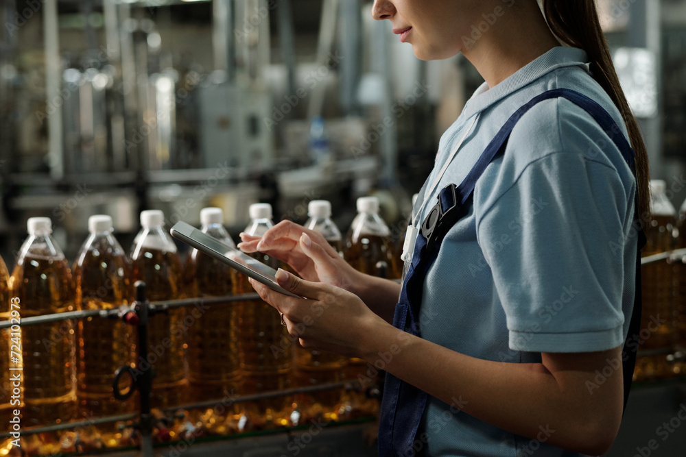 Aufkleber Tablet in hands of young quality inspector standing in front of line with capped plastic bottles with soda or lemonade in factory