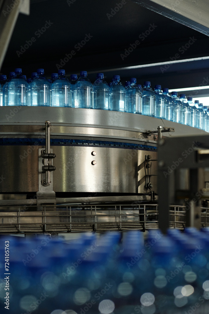 Aufkleber part of production line of filtered bottled mineral water moving on conveyor belt inside large facto