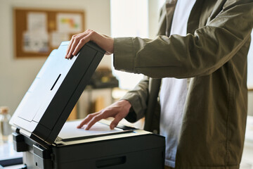 Cropped shot of young businessman putting paper on copier screen of xerox machine to make some...
