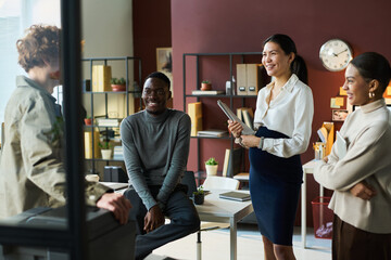Group of young happy intercultural office managers in quiet luxury attire standing in coworking space and discussing working points