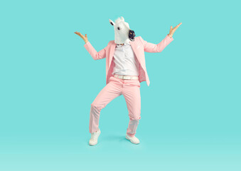 Full length photo of a funny man wearing bright pink suit in animal head horse mask having fun on studio blue background. Entertainment, party, humor and creative advertisement concept.