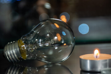 A candle burns near an incandescent light bulb, the price of electricity