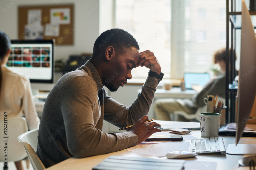 Poster side view of young bored african american manager or designer scrolling in mobile phone while sittin