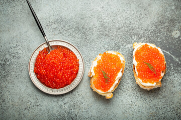 Small metal plate with red salmon caviar and two caviar toasts canapé on grey concrete background,...