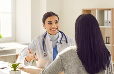 Obraz premium Smiling doctor discussing treatment with female patient in medical office. Therapist, general practitioner with stethoscope consulting young woman during medical checkup visit