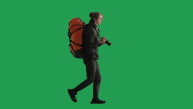 Side view of a male traveler taking photos on a camera during a hike. Man hiker in full length walking in studio on green screen. Concept of travel, active rest, hiking.