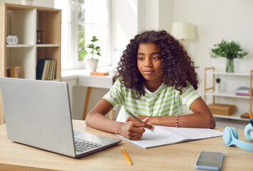 Smiling African American Girl studying with laptop computer. Teenage girl sitting at her desk and...