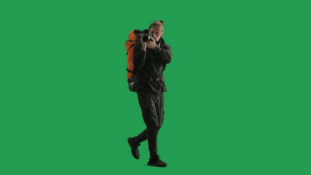 A male traveler takes pictures with a camera while hiking. Man hiker in full height walking in studio on green screen. Concept of travel, active rest, hiking.