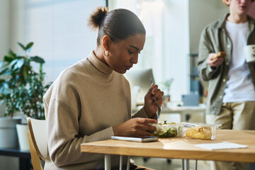 Young hungry African American female white collar worker sitting by table at lunch break and having...