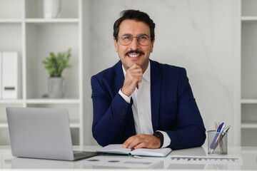 Naklejka premium Smiling confident caucasian adult businessman in suit at table with computer laptop