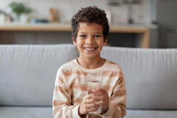 Cheerful little black boy with bright smile holding clear glass of water - Powered by Adobe