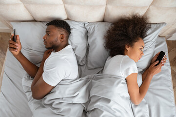 Young Black Couple Texting Lying Back To Back In Bedroom - obrazy, fototapety, plakaty
