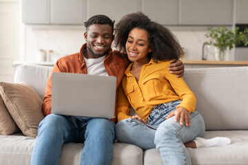 Happy Black Couple Embracing Browsing Internet On Laptop At Home