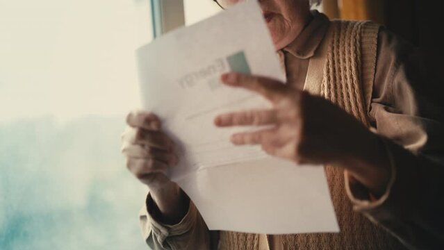 Surprised senior woman reading a letter, shocked by expensive energy bill