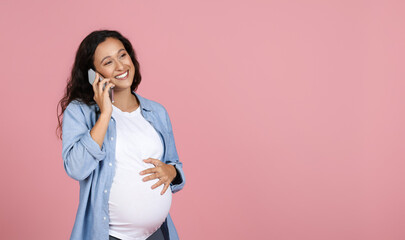 Positive young woman expectant talking on phone, pink background