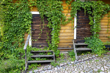 Ivy-covered yellow wooden house on cobblestone street. Porvoo, Finland. - 724131925