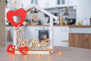 Key to tiny house of cozy home with Valentine decor on table of kitchen. Gift for valentines day, family love nest. design, project, moving to new house, mortgage, rent and purchase real estate