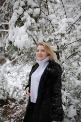 beautiful forty-year-old woman in a snowy forest. a woman in a fur black fur coat in winter in the forest. middle-aged woman near snowy trees