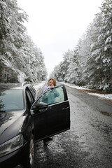 beautiful forty-year-old woman in a snowy forest. a woman in a fur black fur coat stands near a black car in winter in the forest. middle-aged woman and a car