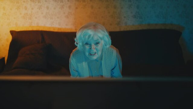 Senior woman watching news and talking to the TV, criticizing authorities
