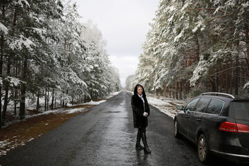 beautiful forty-year-old woman in a snowy forest. a woman in a fur black fur coat stands near a black car in winter in the forest. middle-aged woman and a car