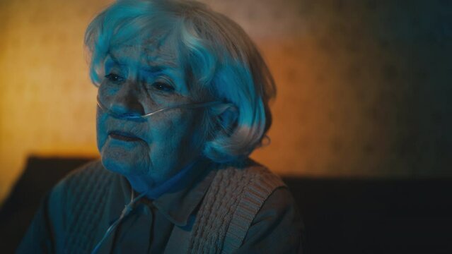 Pleased elderly woman with nasal cannula watching TV show in the evening