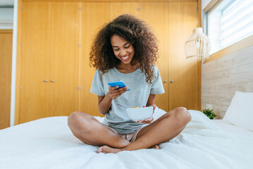 Woman sitting on bed with mobile phone and bowl
