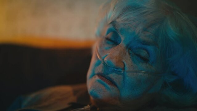 Tired senior woman with nasal cannula napping on couch in front of tv, fatigue